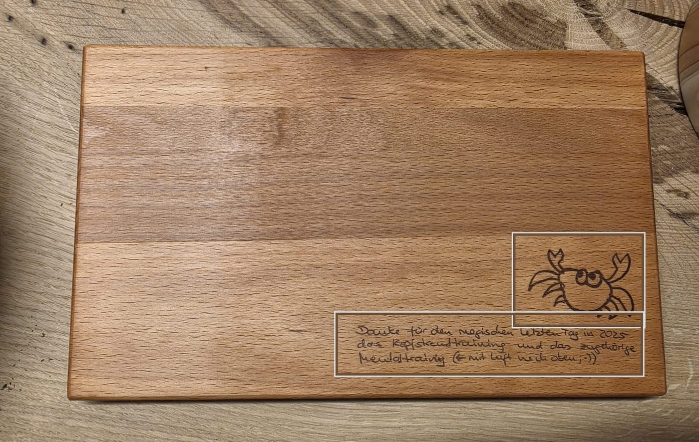 Ein Schneidebrett aus Buchenholz von oben. Unten rechts sind eine gezeichnete Krabbe und drei Zeilen Handschrift eingraviert, beide mit einem feinen Rahmen markiert.