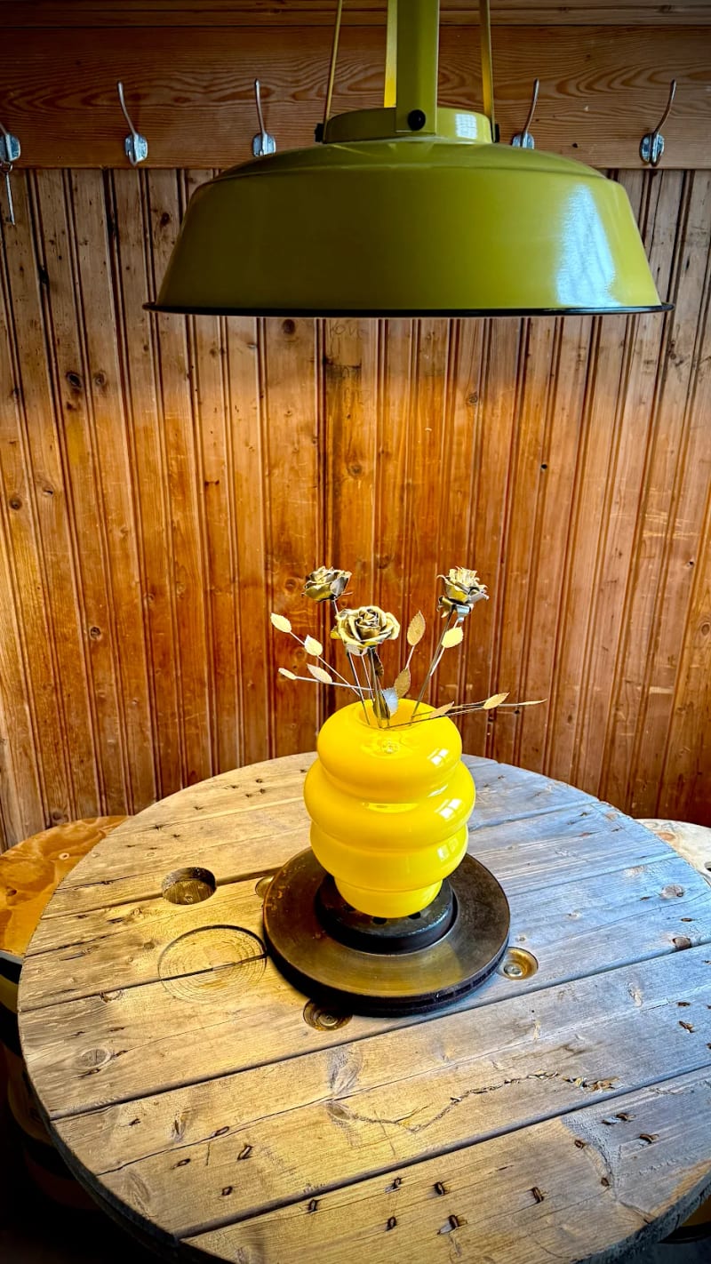Die Metallrosen in der gelben Vase auf dem Holztisch unter der Lampe
